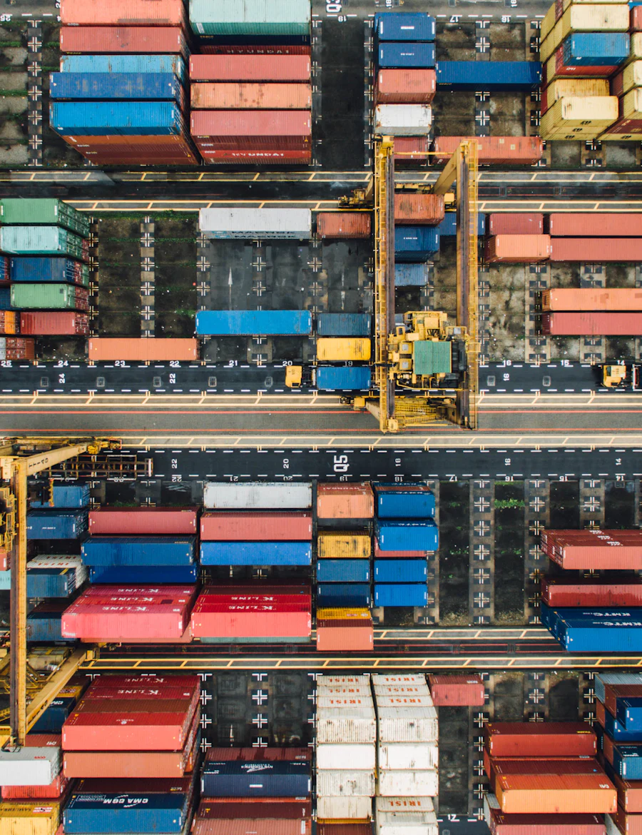 Rows of coloured shipping containers and cranes at a port, seen from above